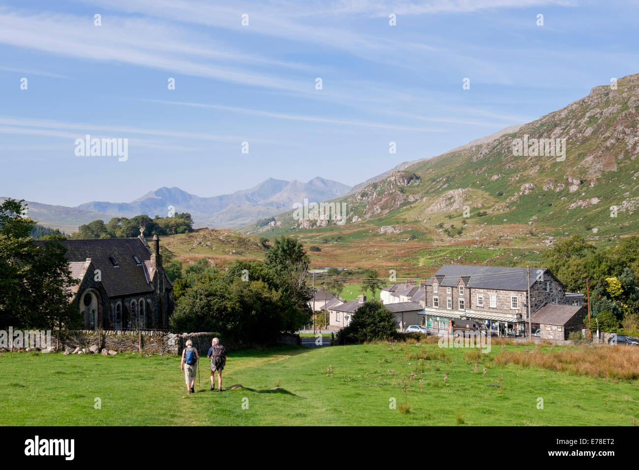 View to the rural village with two walkers walking down the hillside In Snowdonia National Park. Capel Curig, Conwy, North Wales, UK, Britain Stock Photo