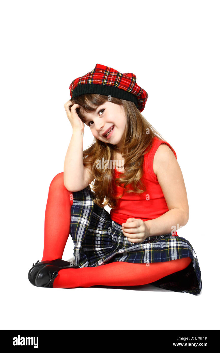 Pretty little girl sits dressed in Scottish style. Portrait on white background with shadows Stock Photo