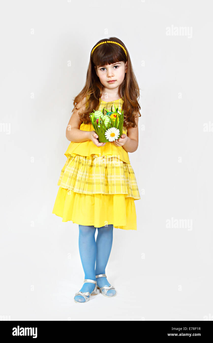 Cute little girl in yellow poses with easter nest in hands. Ful height portrait on natural gray background Stock Photo