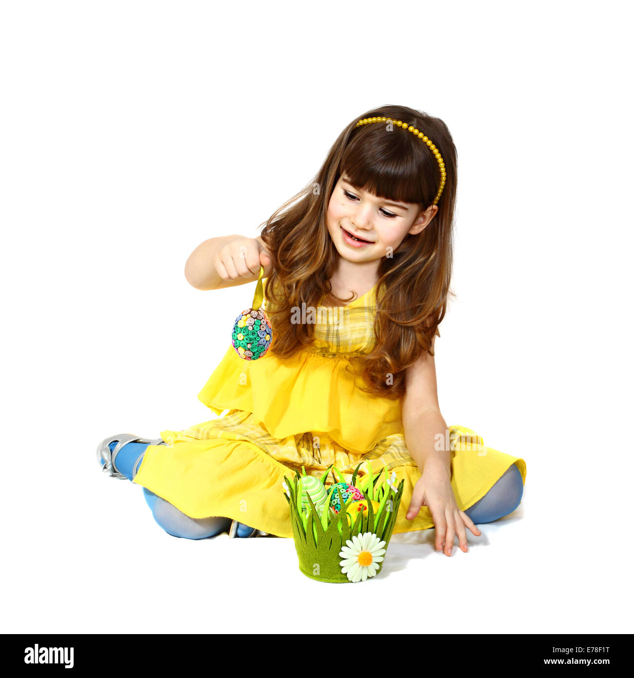 Cute little girl in yellow dress sits and plays with easter egg. Portrait on white background with shadows Stock Photo