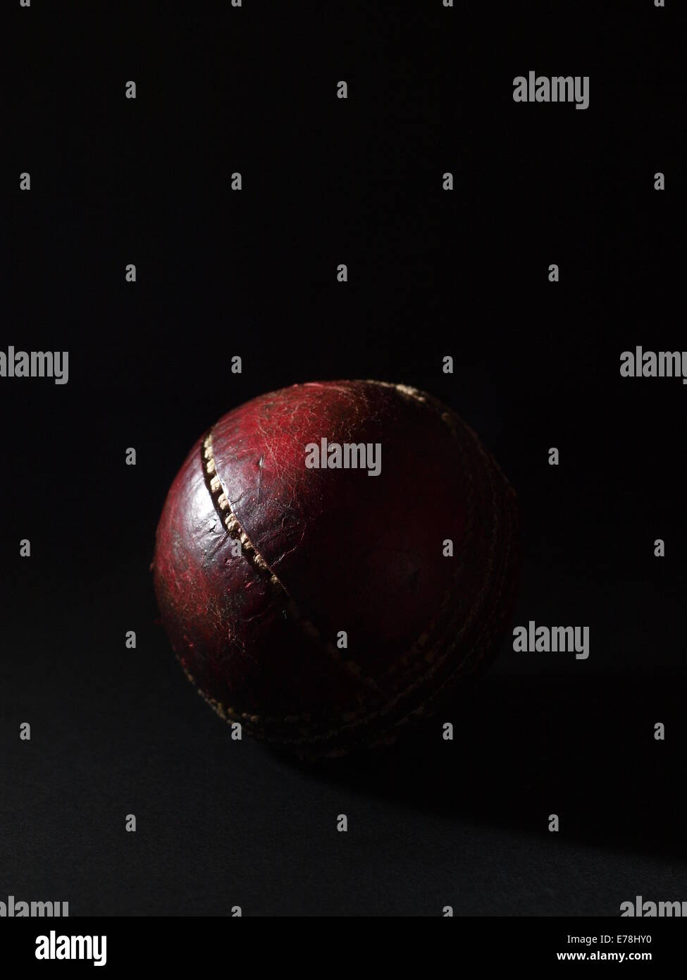 Old, red leather cricket ball with stitching coming apart on black background Stock Photo