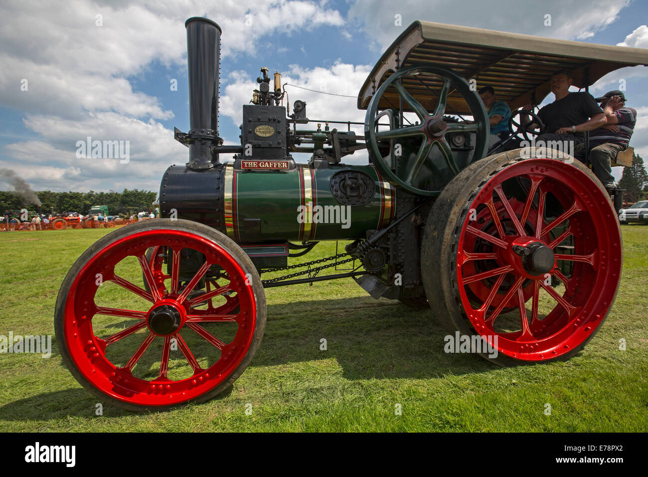 Immaculately restored steam traction engine with gleaming red and green paintwork driven by man at English country fair. Stock Photo