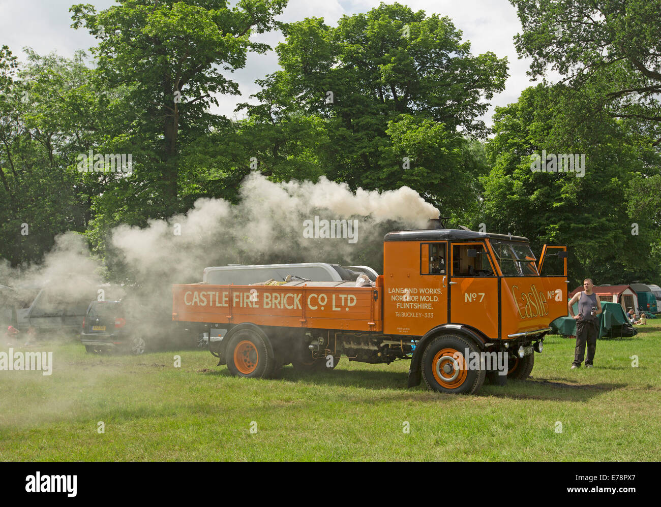 Immaculately restored steam lorry with bright orange paintwork puffing out smoke and on display at English country fair Stock Photo