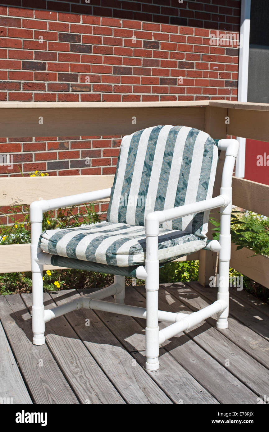 A generic lawn chair constructed with white PVC piping and plastic cushions  on a wood deck with a brick wall in the background Stock Photo - Alamy