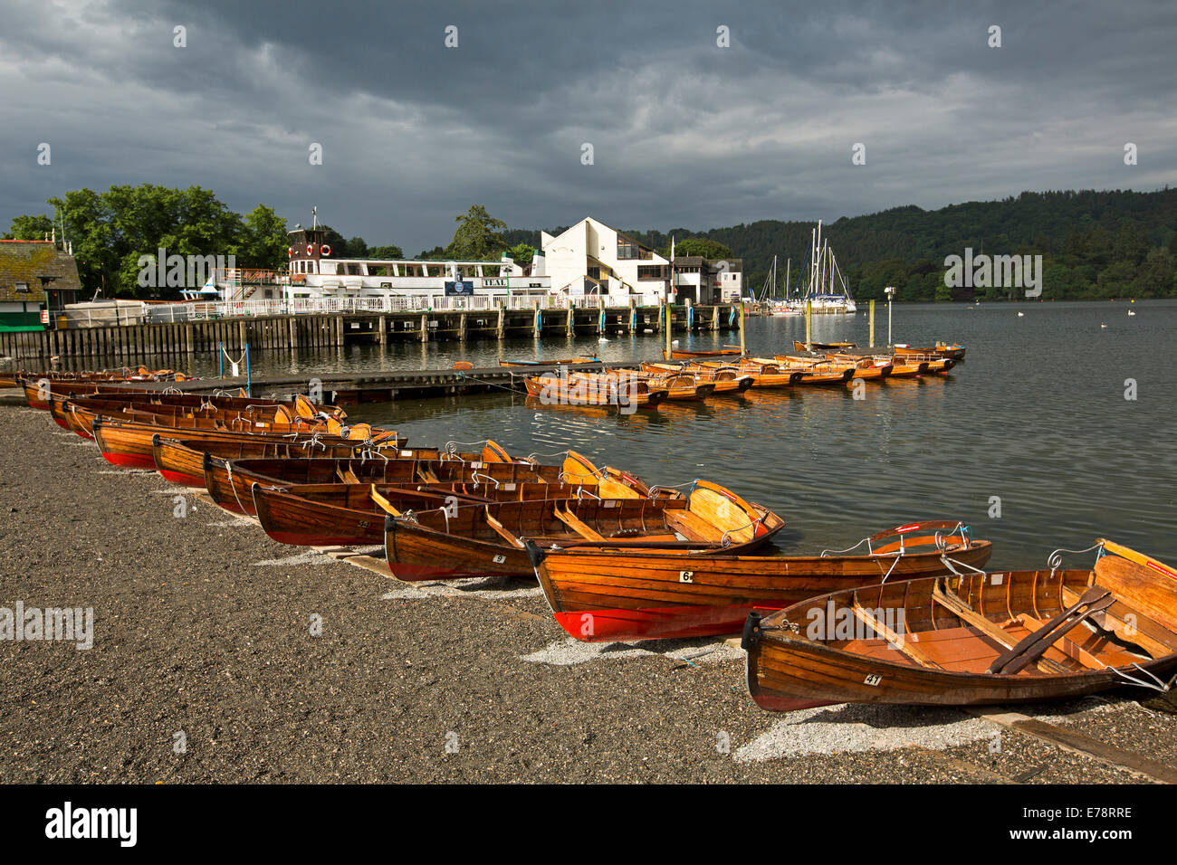 Row of colourful wooden rowing boats on bank of Lake Windemere under stormy sky in Cumbria England Stock Photo