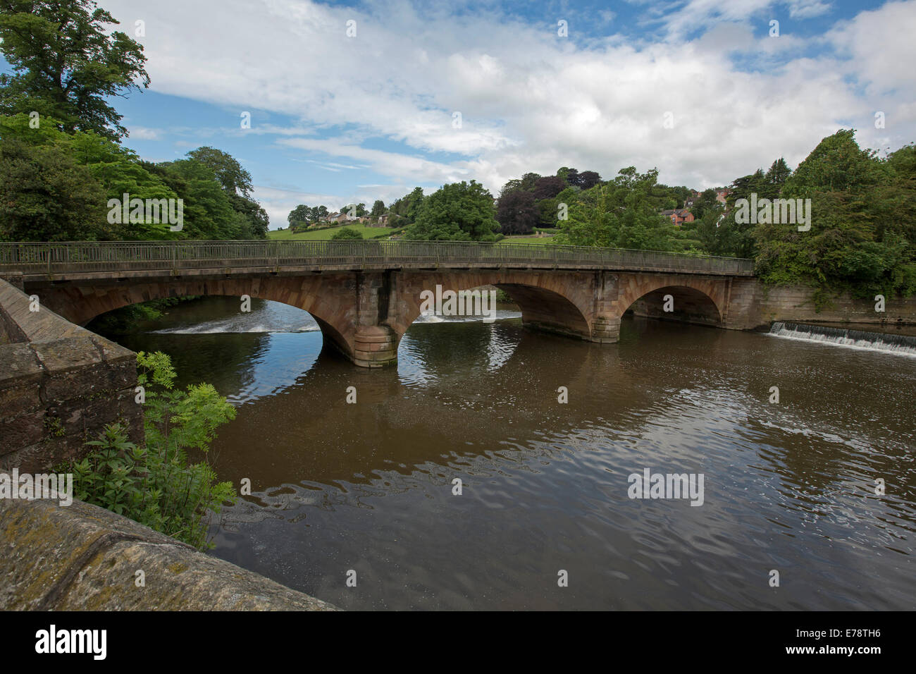 Ornate arched bridge over River Derwent, with bridge, trees, and blue sky reflected in calm water at English village of Belper Stock Photo