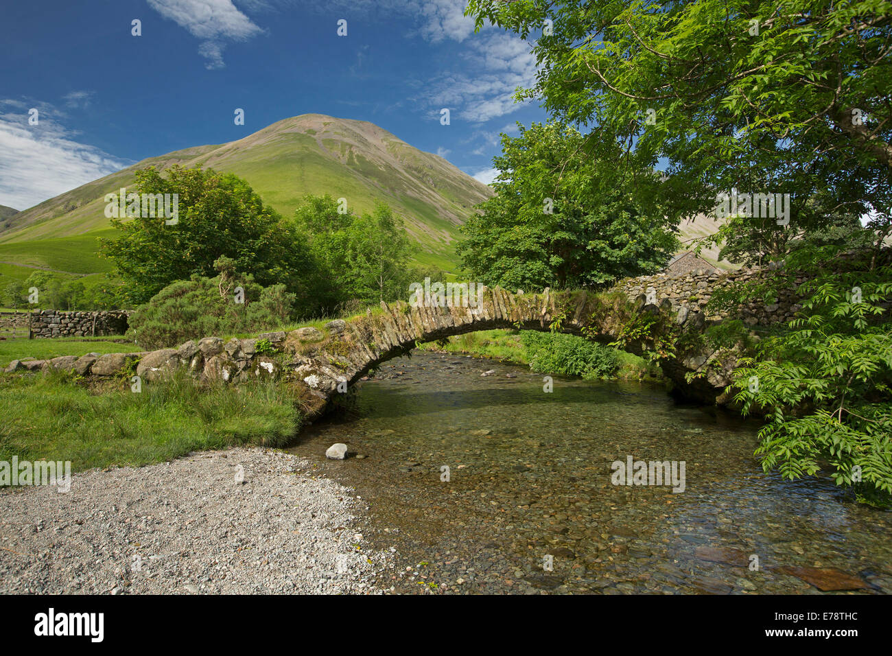 Landscape with high mountain peak, blue sky, arched stone pedestrian bridge over clear shallow stream at Wasdale Head, Lake District Cumbria England Stock Photo
