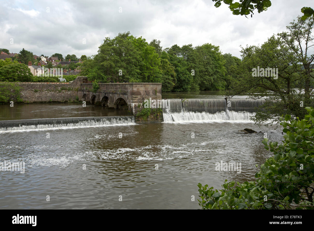 Derwent River spilling over horseshoe shaped weir at English village of Belper with riverbank trees reflected in calm water Stock Photo