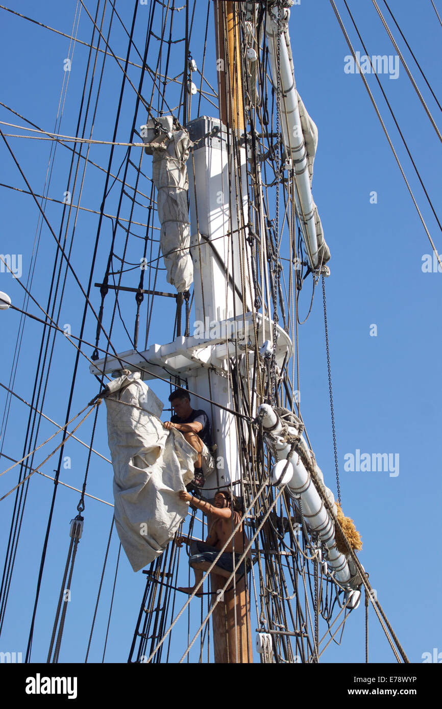 Crew members work high up in the rigging of a tall ship adjusting the ...