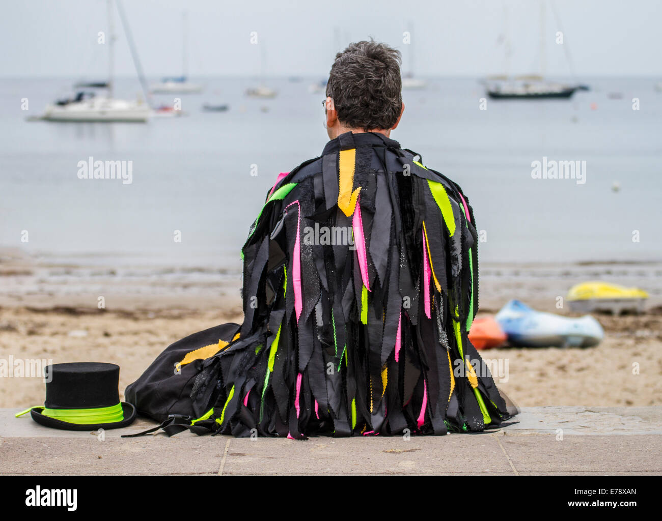 Traditional morris dancer sitting on side walk looking into bay with yachts with hat by his side Stock Photo