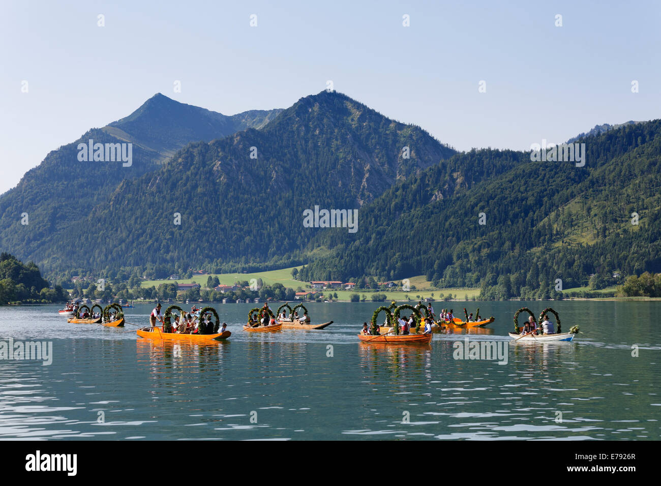 Locals wearing traditional costumes in decorated wooden Plätte boats, Brecherspitz mountain at the back, Stock Photo
