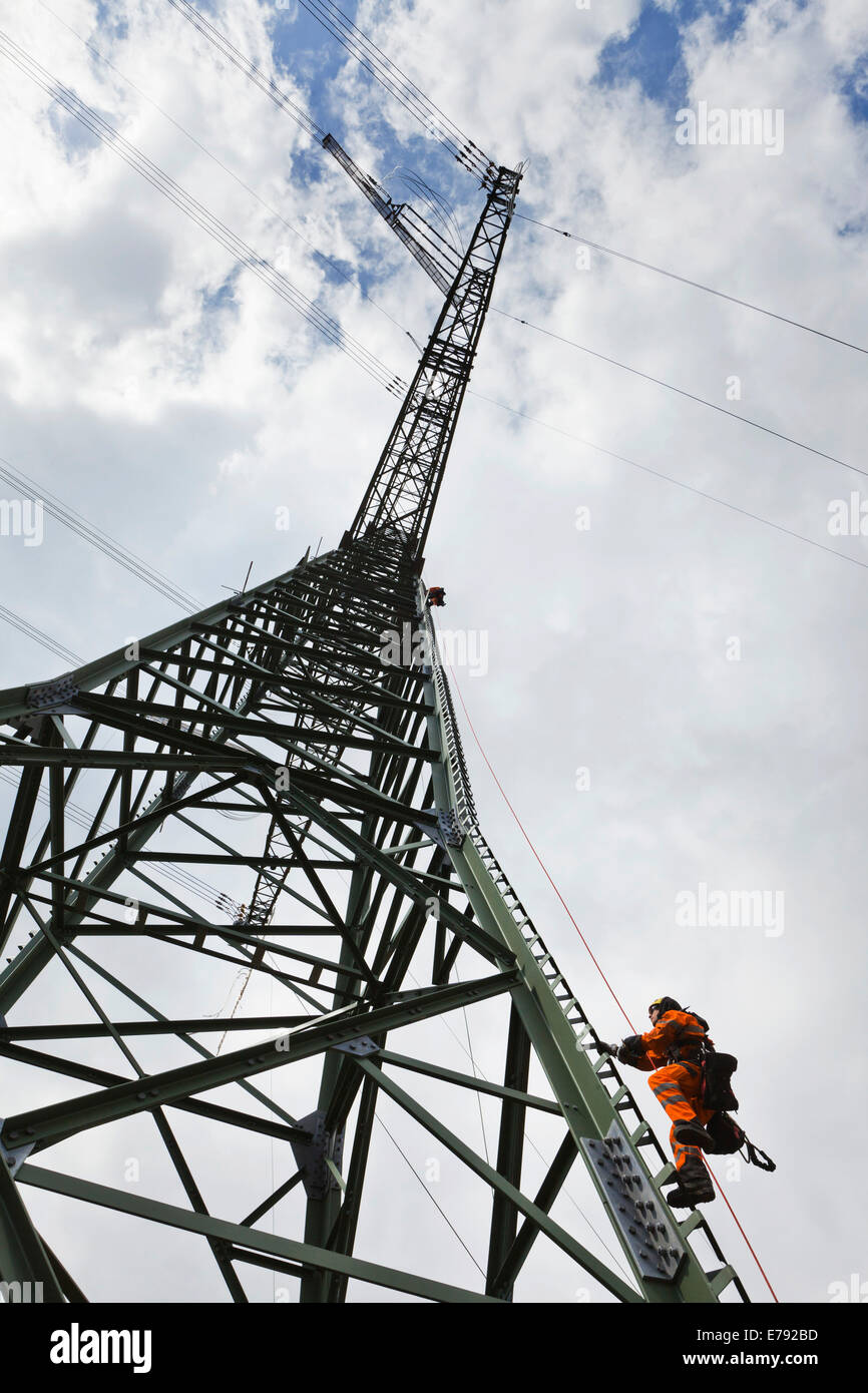 Overhead transmission cable installer climbing a mast to install insulated cable on a newly built high-voltage transmission mast Stock Photo