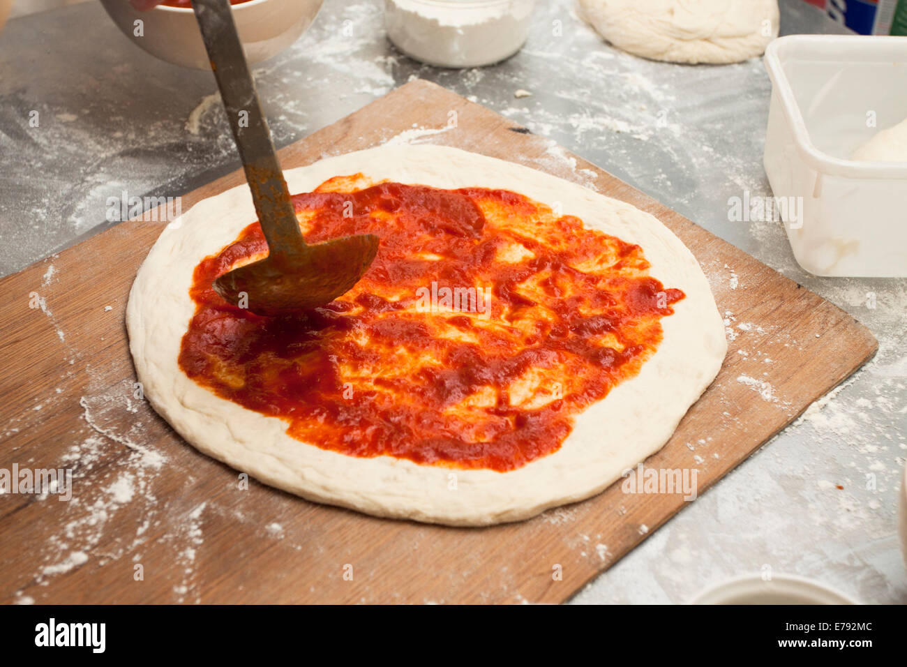 Spreading fresh tomato sauce on homemade pizza with sourdough crust