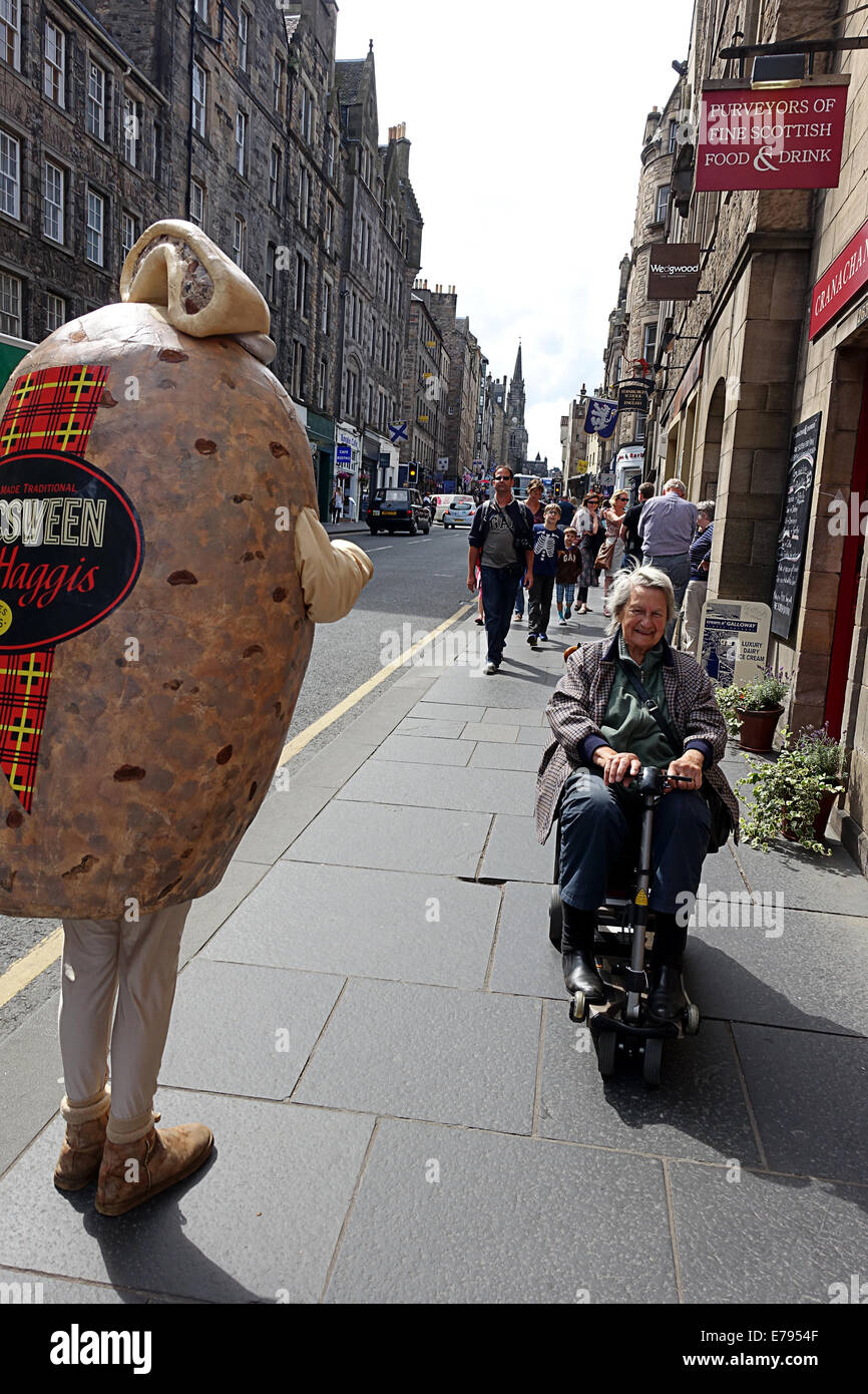 Lady on mobility scooter passing man dressed as a Haggis. Canongate The