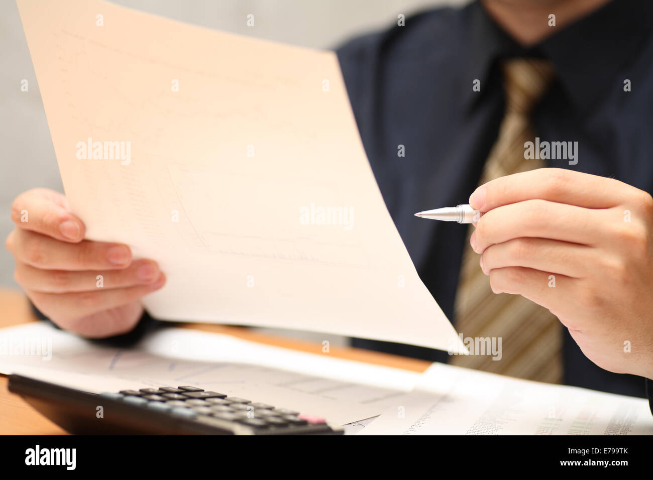 Businessman viewing financial statements. Shallow depth of field. Focus on hand and pen. Close-up. Stock Photo