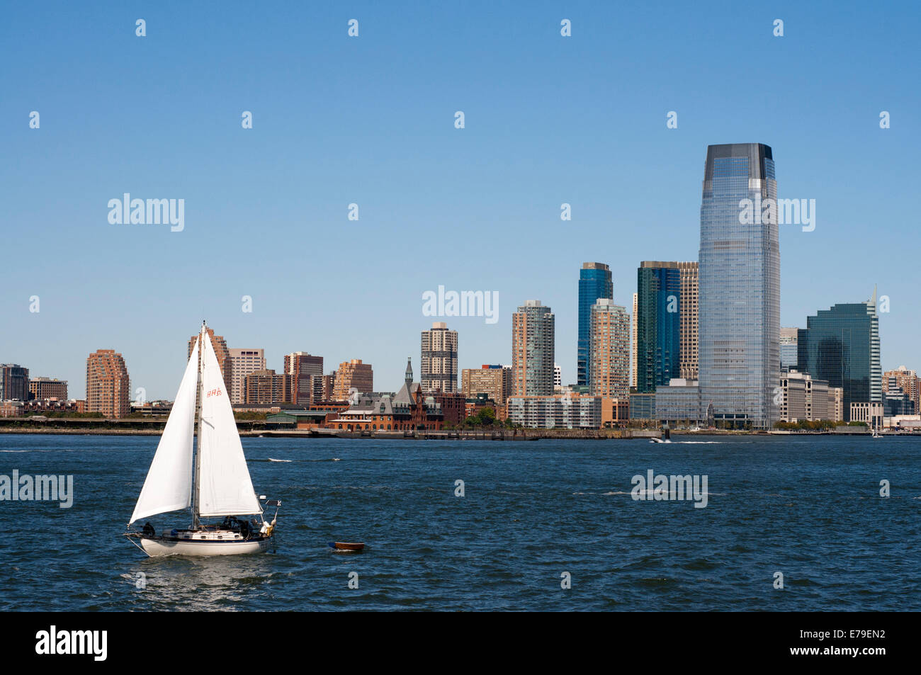 Battery Park City. A large green area with a promenade along the Hudson River, beginning at the southern tip of Tribeca, in Rockefeller Park and extends to the Ferry Terminal on Staten Island, sharing the stage with modern buildings in which live the jet-set New York. The photo shows a sailing boat around the bay and some buildings at the back of Jersey. Stock Photo