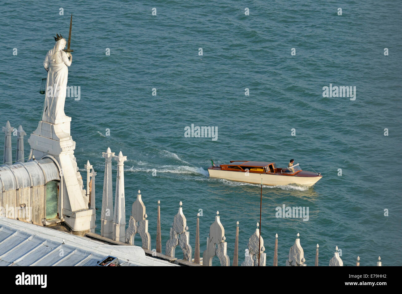Statue on the Doges Palace facing the Venetian lagoon, as a small motorboat passes Stock Photo