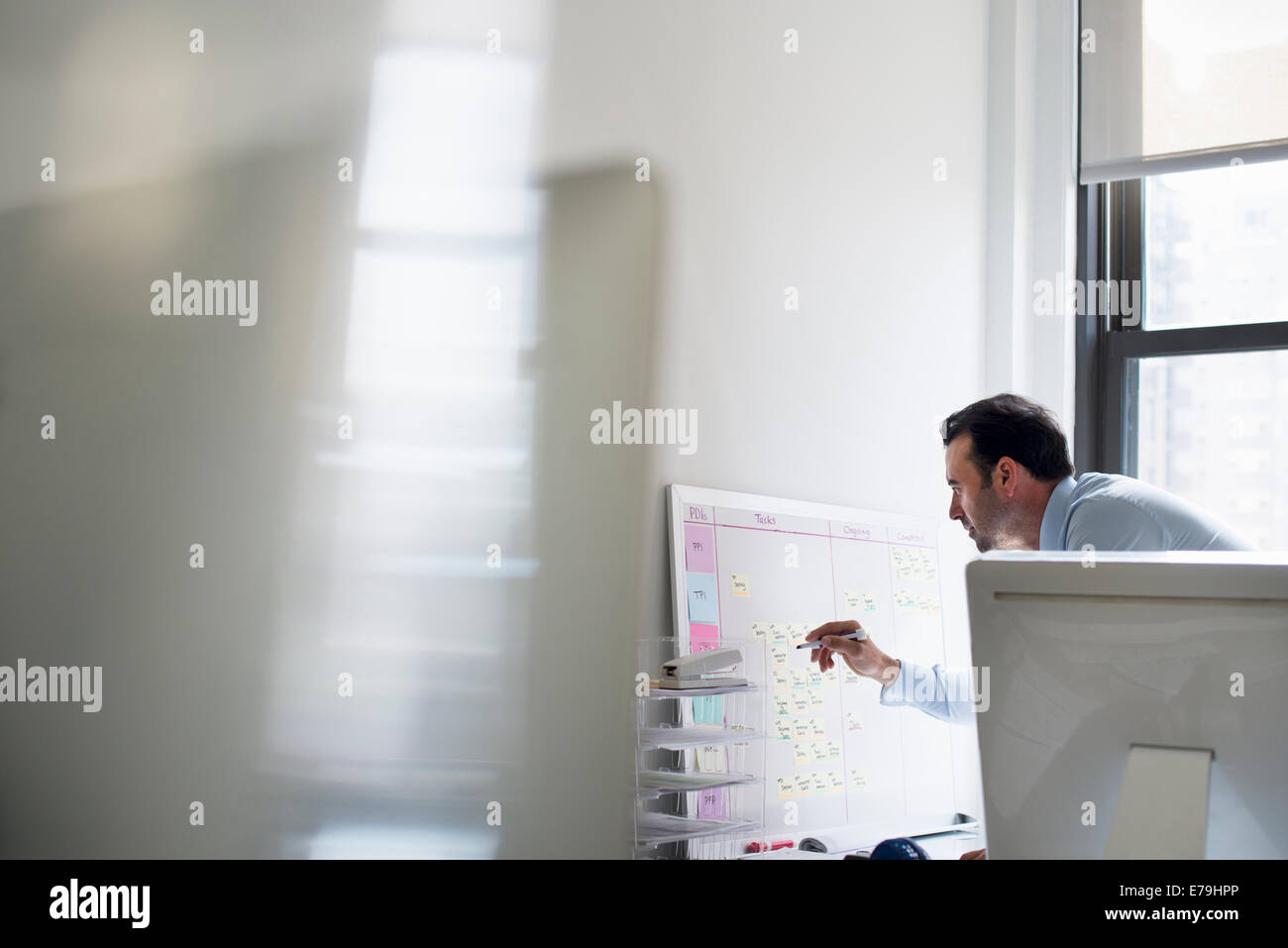 A man using a pen to mark a wall chart or project plan on an office