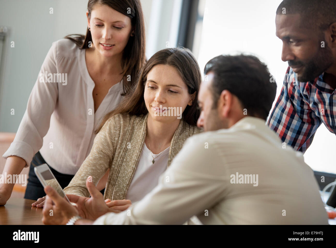 Four people, men and women, grouped around a digital tablet, looking at the screen. Stock Photo