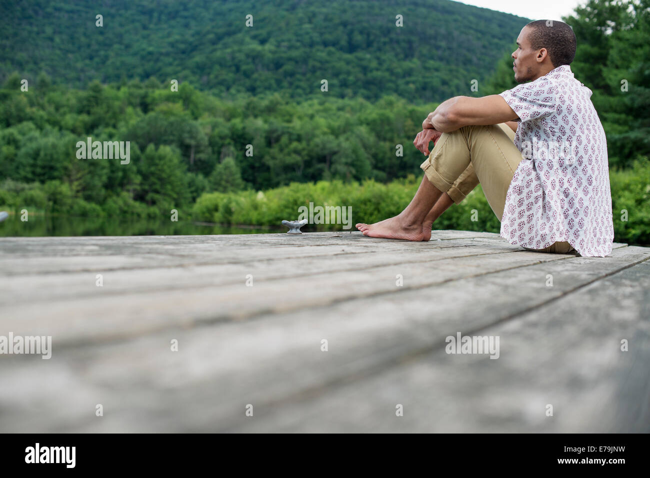 A man sitting on a wooden pier by a lake in summer Stock Photo