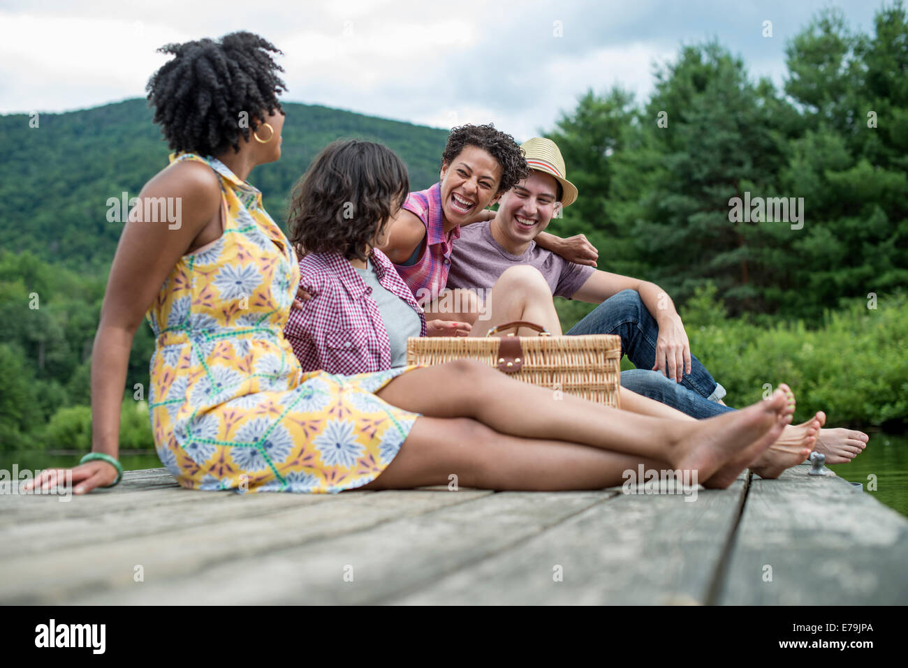 A group of people sitting on a woode pier overlooking a lake. Stock Photo