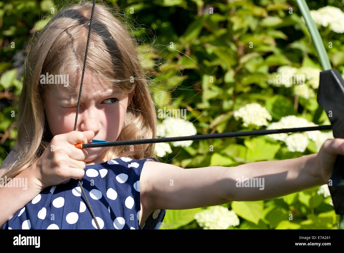 little caucasian girl aiming arrow from big bow on outdoor nature background Stock Photo