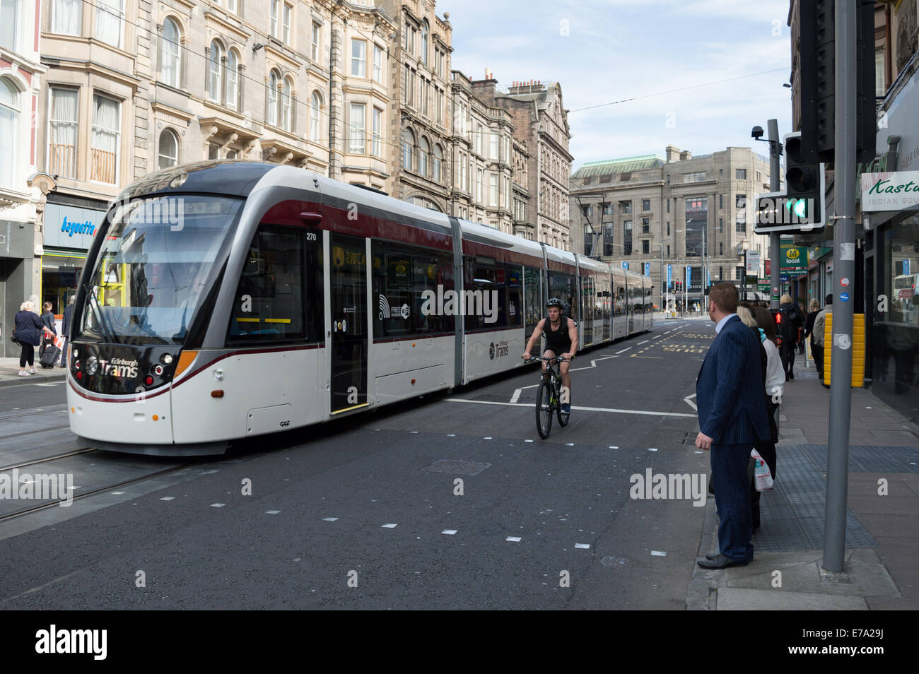 People waiting at a pedestrian crossing with tram and cyclist passing Stock Photo