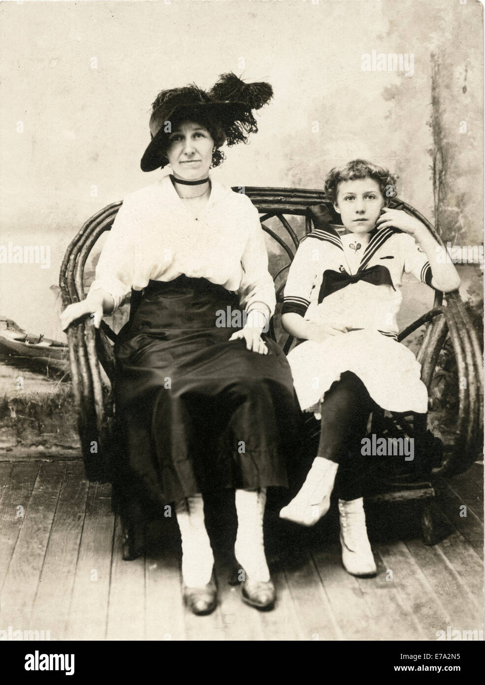 Woman in Black Hat with Teenage Girl in Sailor Outfit Sitting on Rattan Chair, Portrait, circa 1910 Stock Photo