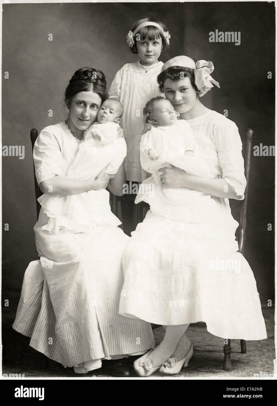 Two Seated Women Holding Newborn Infants with Young Girl Standing in Rear, Portrait, circa 1920 Stock Photo