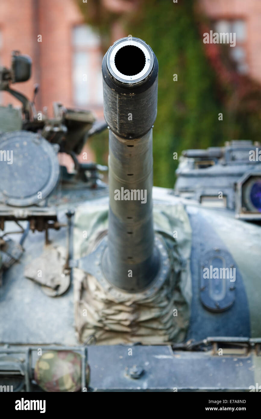 War tank turret closeup. A barrel of a military tank pointed to the sky. Old barrack building on the background. Stock Photo