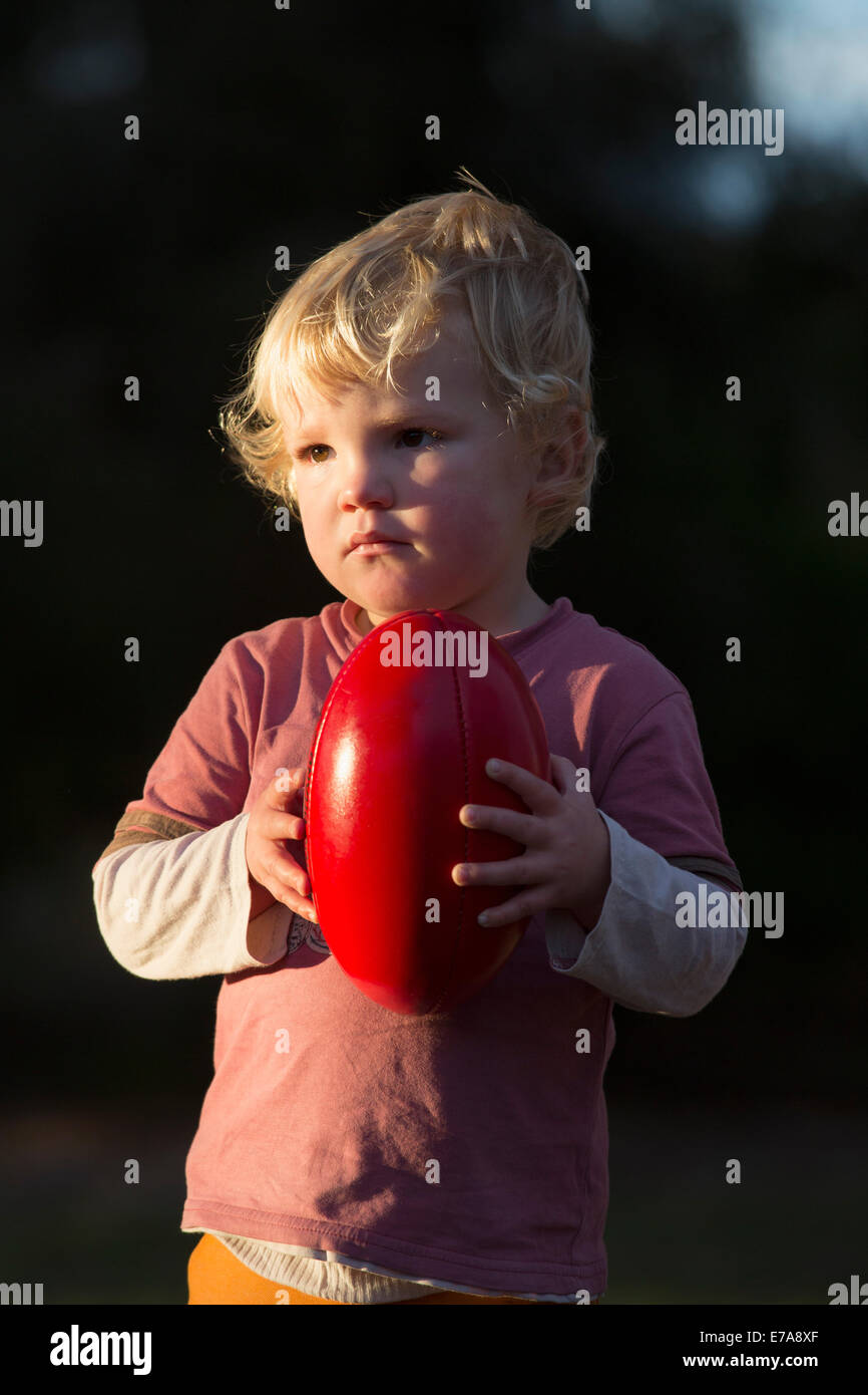 Cute boy looking away while holding a football outside Stock Photo