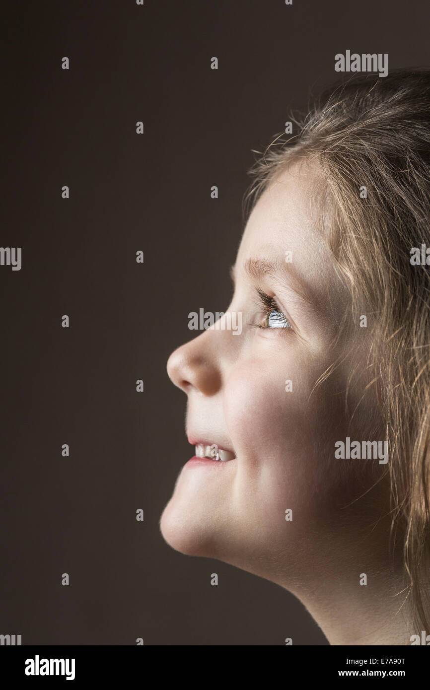 Close-up side view of smiling girl looking up over gray background Stock Photo