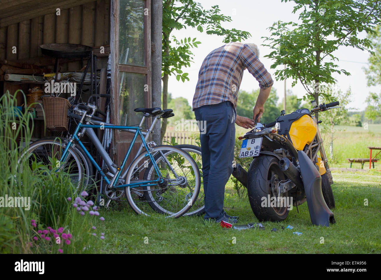 Rear view of mature man repairing motorcycle at yard Stock Photo