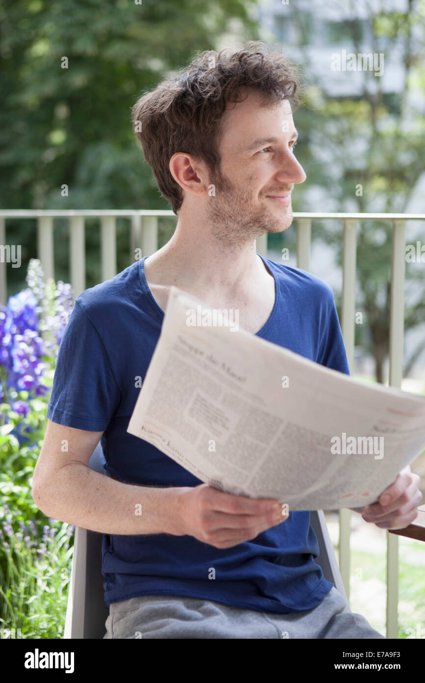 Young man looking away while holding newspaper at porch Stock Photo