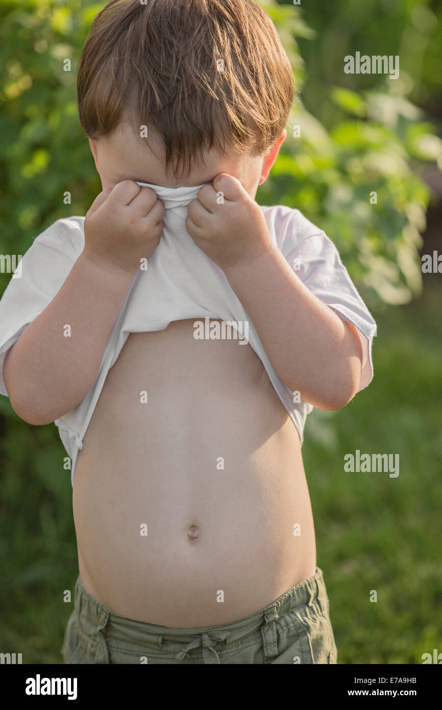 Young boy covering face with t-shirt in park Stock Photo