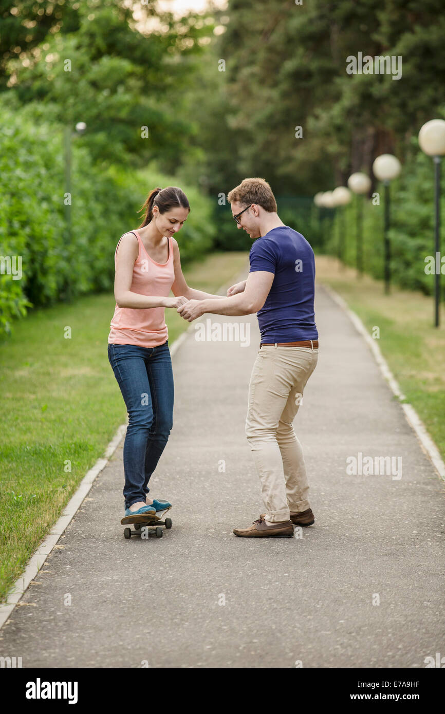 Man assisting woman in skate boarding on footpath Stock Photo