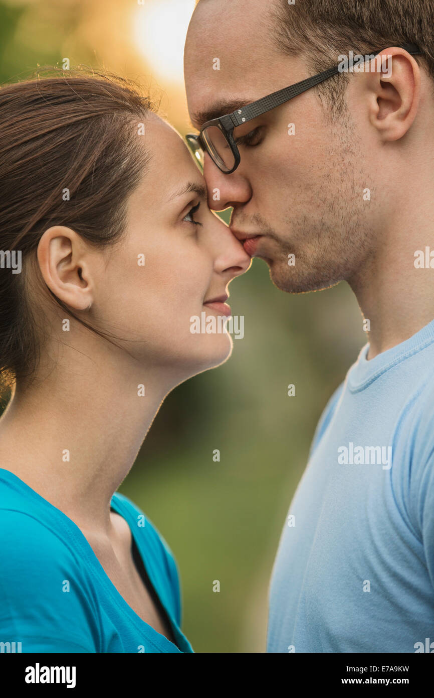 Side view of young man kissing woman on nose in park Stock Photo