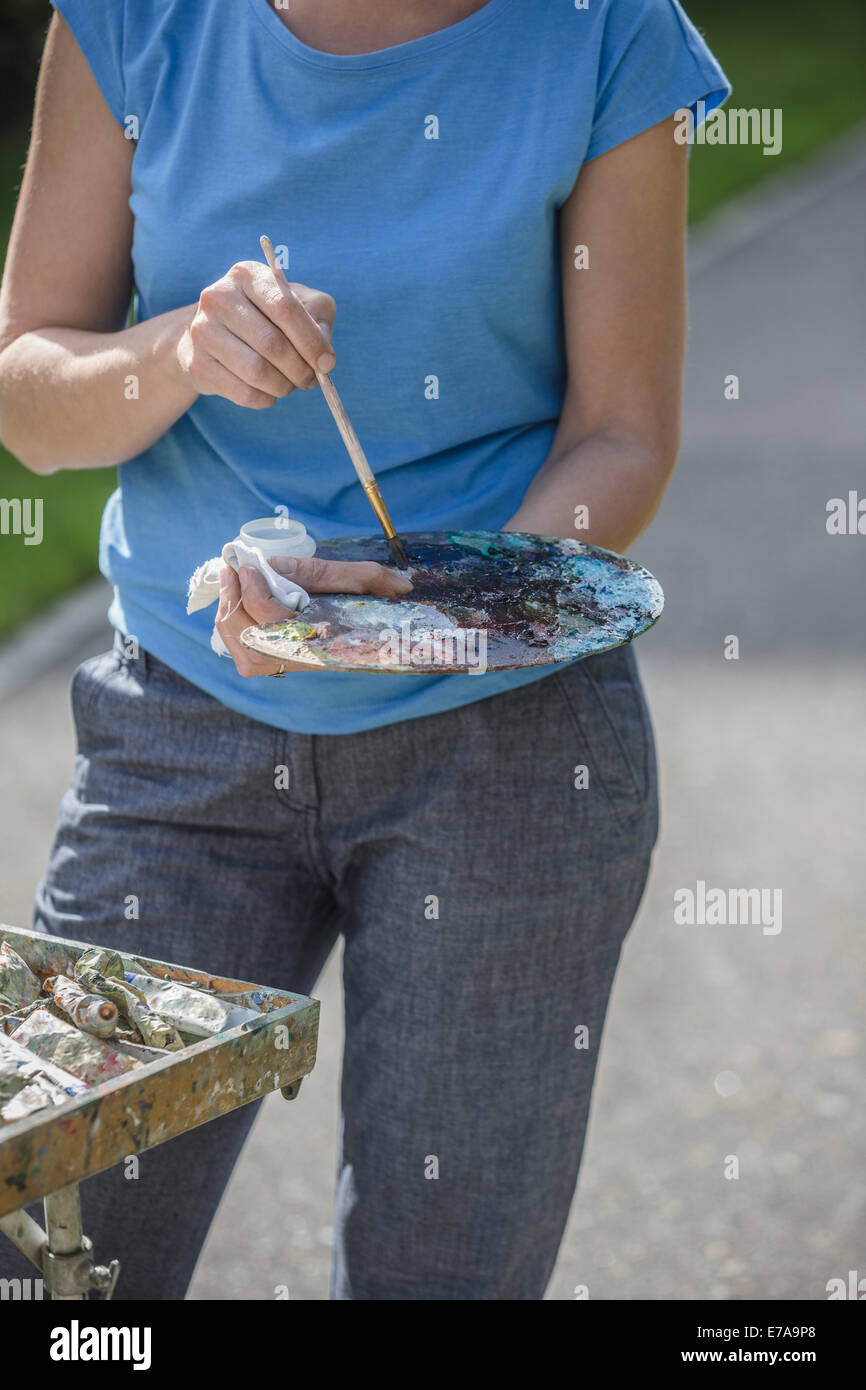 Midsection of female painter holding paintbrush and palette in park Stock Photo