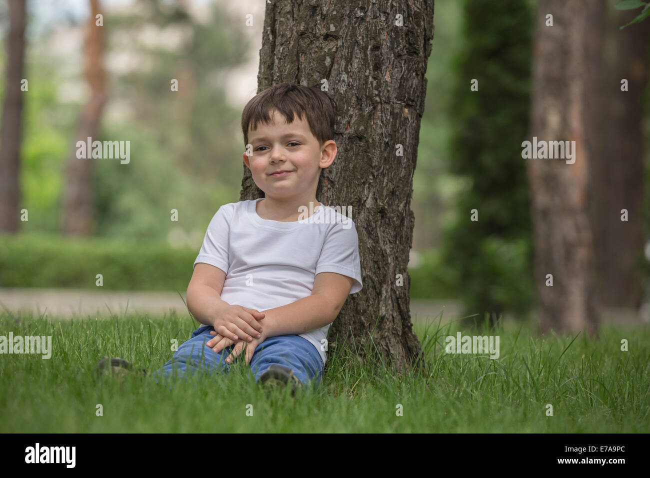 Portrait of cute boy relaxing against tree in park Stock Photo
