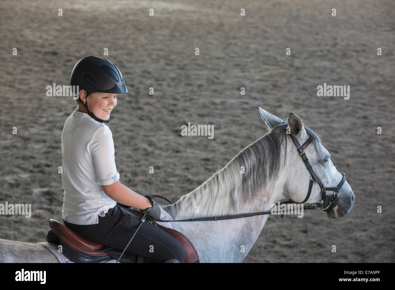 Side view of boy sitting on horse in training stable Stock Photo