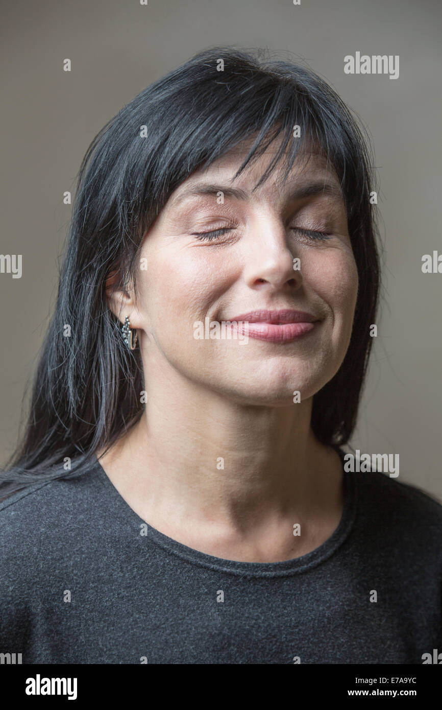 Smiling mature woman with eyes closed against gray background Stock Photo