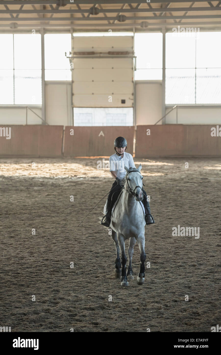 Little boy riding horse in training stable Stock Photo