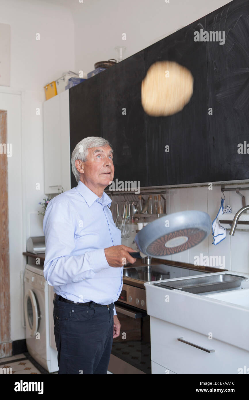 Senior man tossing pancake on frying pan in kitchen at home Stock Photo