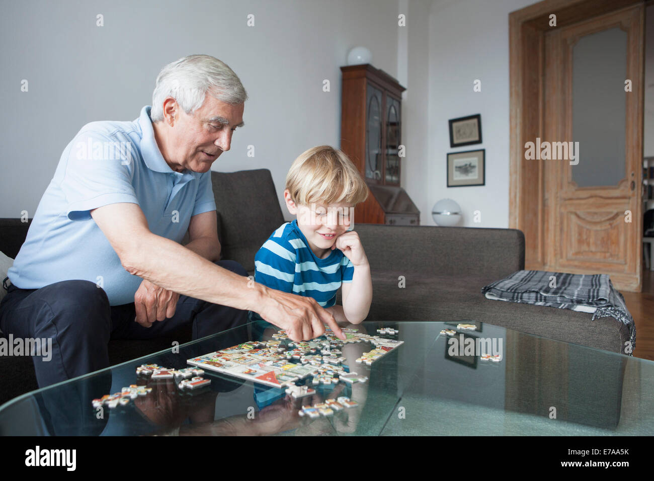 Grandfather solving jigsaw puzzle with grandson in living room at home Stock Photo