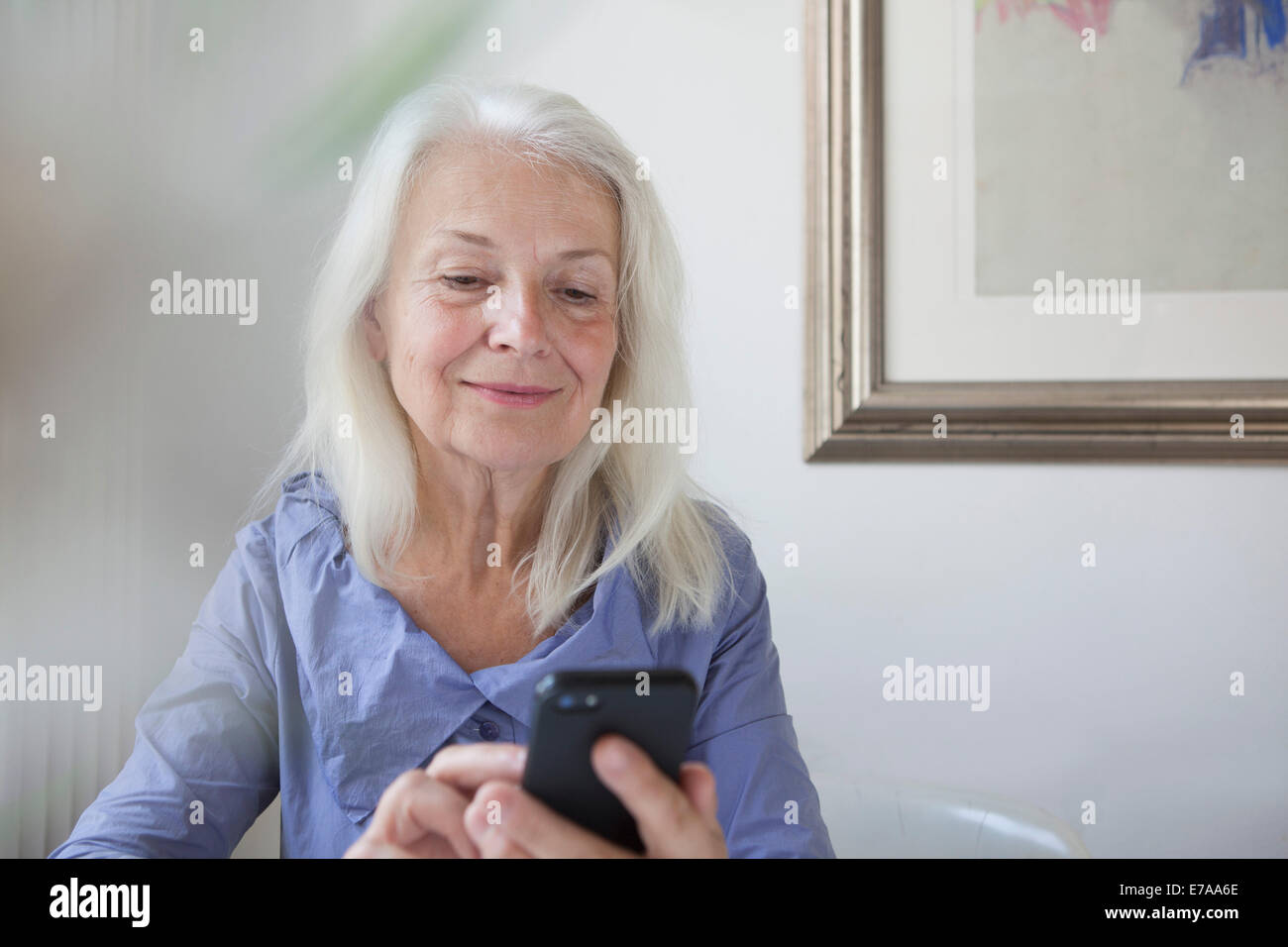 Senior woman text messaging through smart phone at home Stock Photo