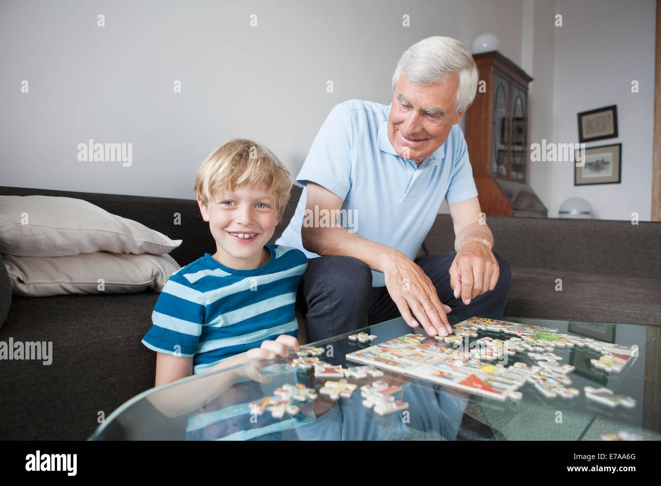 Portrait of happy grandson solving jigsaw puzzle with grandfather in living room at home Stock Photo