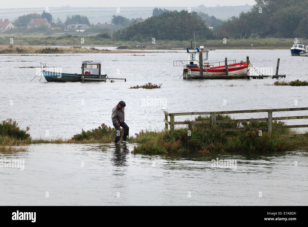 Thornham, Norfolk, UK. 11th Sept 2014. An exceptionally high tide floods the harbour, Staithe Road and the marshes at Thornham causing a little difficulty for a stranded walker. Credit:  Stuart Aylmer/Alamy Live News Stock Photo