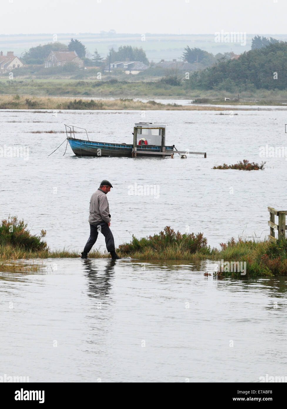 Thornham, Norfolk, UK. 11th Sept 2014. An exceptionally high tide floods the harbour, Staithe Road and the marshes at Thornham causing a little difficulty for a stranded walker. Credit:  Stuart Aylmer/Alamy Live News Stock Photo