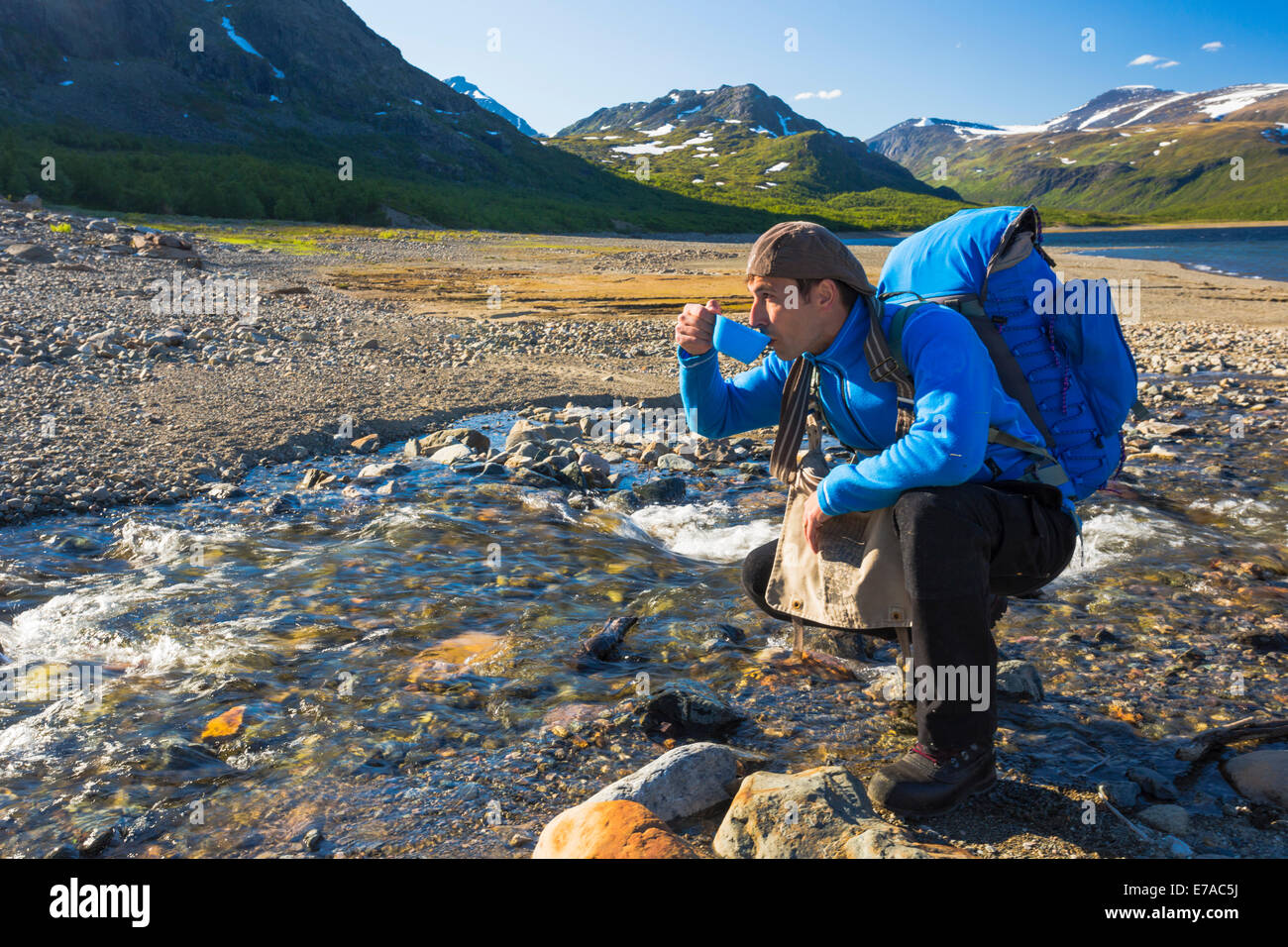 White man hiking and drinking water from a creek in stora sjöfallets