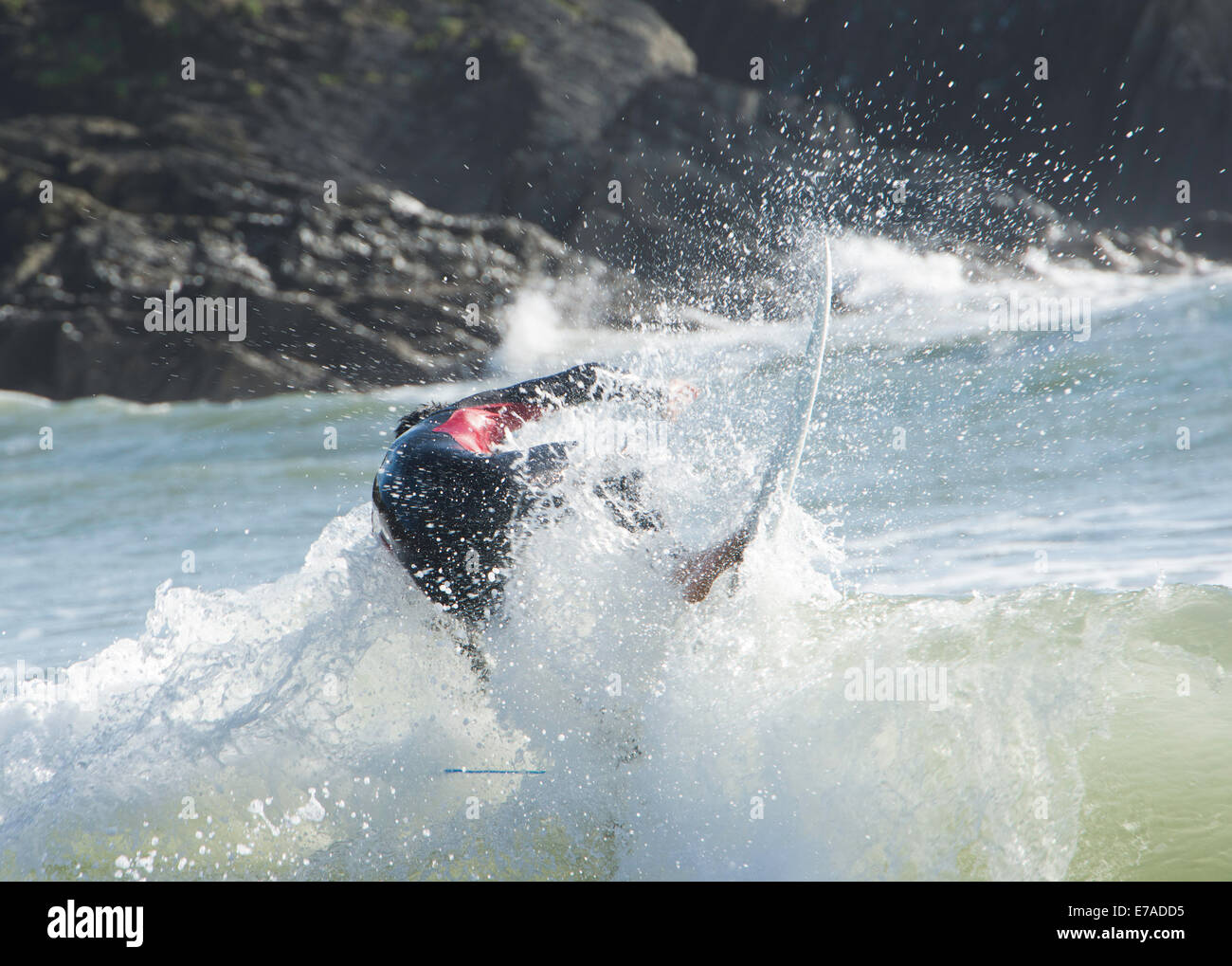 Action shot of surfer riding wave with rocks in background Stock Photo